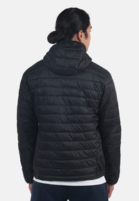 Giacca a vento nera con cappuccio, caratterizzata da un design trapuntato, texture liscia e polsini elastici. La vista posteriore mostra i dettagli di cucitura e una leggera lucentezza.