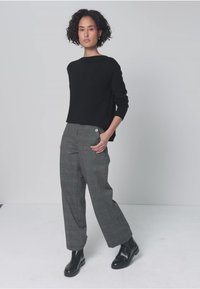 Maglione nero a maglia con maniche lunghe abbinato a pantaloni grigi a quadri a vita alta con bottoni decorativi e stivali neri alla caviglia.