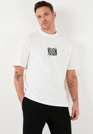 White cotton t-shirt with a graphic black and gray design on the front. Short sleeves and a crew neckline. Textured fabric.