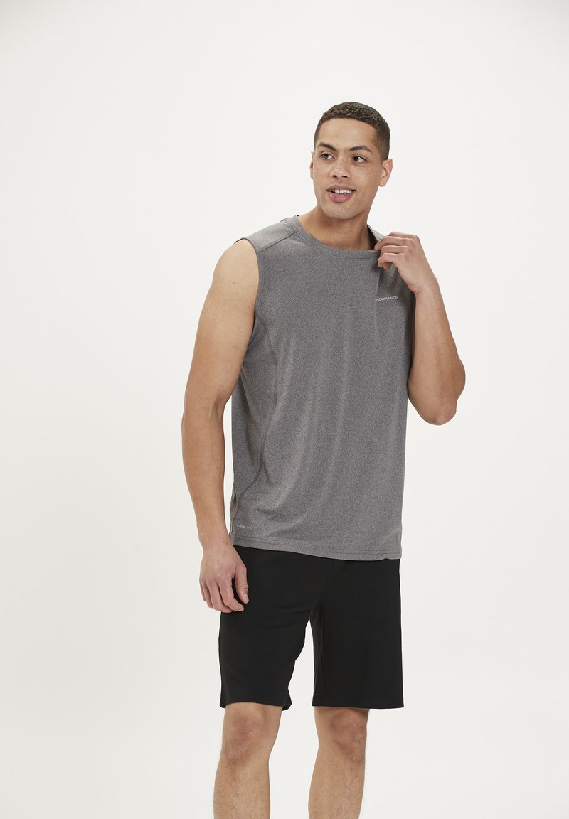 Grijs sportshirt zonder mouwen van vochtafvoerende stof, gecombineerd met zwarte shorts. Bevat een ronde hals en zijscheuren voor ventilatie.