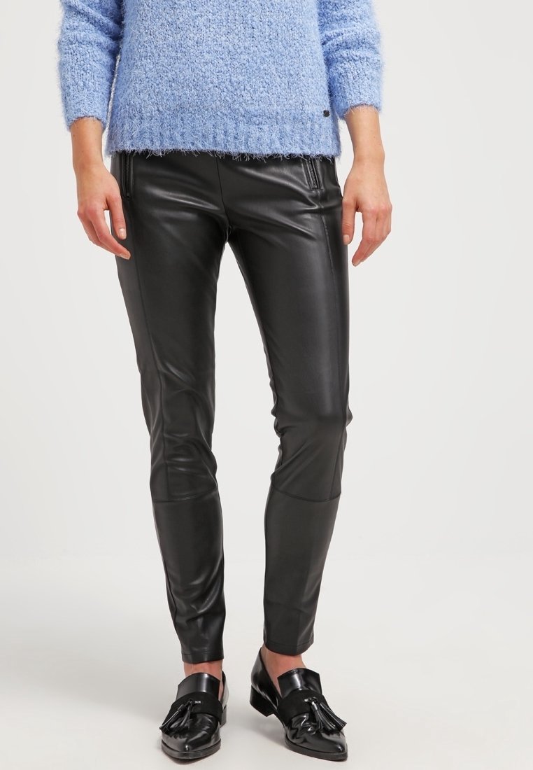 Pantalon en cuir noir avec une coupe ajustée et une texture lisse ; associé à un pull en tricot bleu clair et des mocassins noirs brillants.