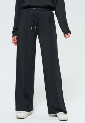 Pantalons larges noirs en tissu doux, dotés d'une taille élastique avec cordons de serrage et de coutures latérales pour un ajustement décontracté.