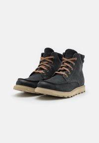 Botas de cuero negro con un acabado texturizado, con cordones marrones, una suela de goma beige y un diseño de media caña para soporte del tobillo.