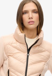 Lys pink pufferjakke med høj krave, lynlåslukning, quiltet tekstur foran og bløde ærmer i et glat materiale.