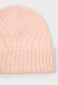 Pink knitted beanie hat with ribbed texture, featuring a folded cuff and subtle embossed logo detail on the front.