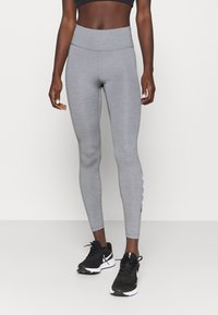 Szare legginsy sportowe z wysokim stanem, dopasowane do sylwetki, z detalami po bokach, w połączeniu z czarnymi butami sportowymi. Gładki, elastyczny materiał.
