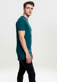 Tirkizna pamučna majica s kratkim rukavima, regularnog kroja i okruglim izrezom, u kombinaciji s crnim slim-fit trapericama s teksturalnim detaljima.
