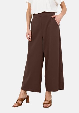 Brune bukser med vide ben og høj talje, med sidelommer og glat tekstur. Kombineret med brune sandaler med hæl.