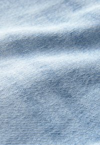 Prim-plan cu țesătură denim albastru deschis, arătând textura țesută detaliată și pliuri subtile.