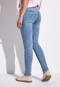 Jean skinny bleu clair avec une texture lisse, dotés de deux poches arrière et d'une taille haute, associés à des baskets fuzzy beige.