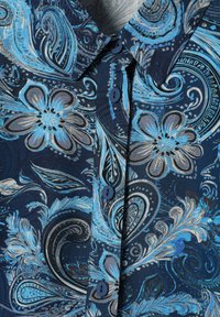 Modrá košeľa s kvetinovým vzorom na námorníckom pozadí, s textúrovanou látkou a modrými gombíkmi pozdĺž zapínania.