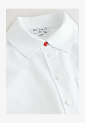 Biała krótka koszulka z krótkim rękawem, z kołnierzykiem w szpic, pięcioma białymi guzikami oraz czerwonym guzikiem w kształcie serca przy dekolcie.