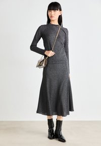 Gray, ribbed knit long-sleeve top paired with a matching mid-length skirt. Model holds a small, metallic handbag and wears black ankle boots.