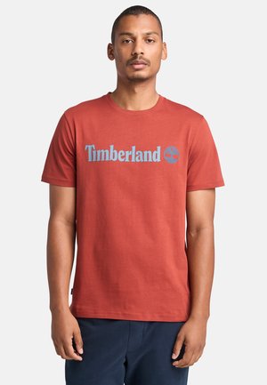 Červené bavlněné tričko s modrým logem "Timberland" a grafikou stromu. Okrúhly výstřih a krátké rukávy s rovnými lemy.