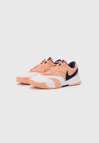 Nike sportsko med en fersken- og hvid overdel med marineblå detaljer, teksturerede overflader og en mønstret gummisål.