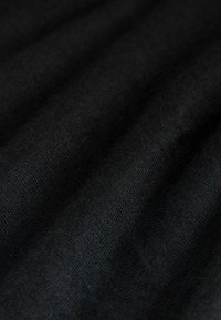 Nahaufnahme von weichem, schwarzem Stoff mit sichtbarer feiner Strickstruktur und sanften Falten, die subtile Schattenmuster erzeugen.