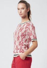 Suéter de punto corto de manga corta en rojo y crema con patrones florales, un cuello acanalado con acentos en negro y crema, y un corte relajado.
