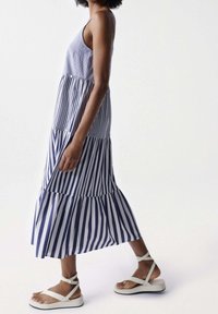Pruhované bezramínkové šaty s vrstveným lemem v námořnické modři a bílé. V kombinaci s lehkými plochými sandály se zkříženými pásky.