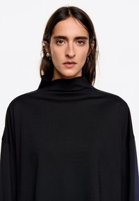 Zwarte coltrui met een relaxte pasvorm, zachte textuur en brede mouwen. Het ontwerp is minimalistisch zonder zichtbare patronen.