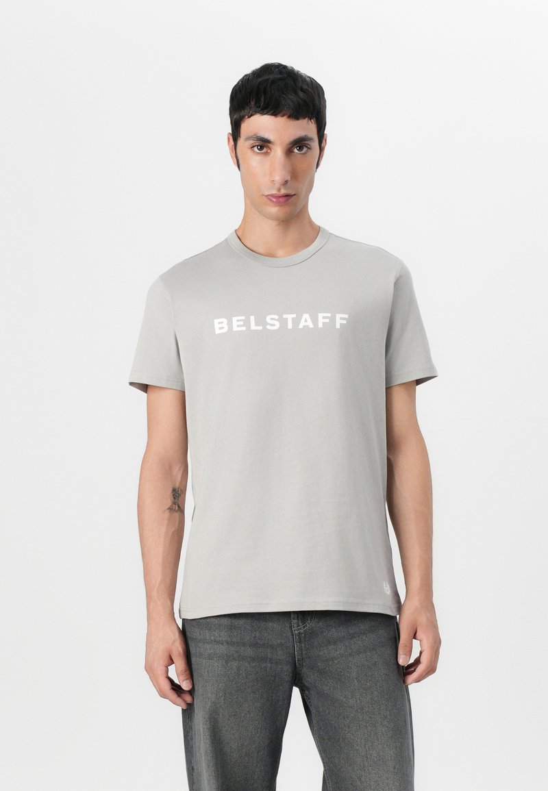 Γκρι βαμβακερό μπλουζάκι με κοντά μανίκια και στρογγυλή λαιμόκοψη. Διαθέτει λευκή επιγραφή "BELSTAFF" στο στήθος. Συνδυάζεται με σκούρες γκρι τζιν.