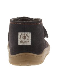 Zwarte stoffen schoen met een brede opening, bruine rubberen zool, gestikte accenten en een wit label met een bomenlogo op de achterkant.
