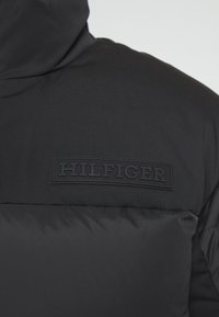 Veste matelassée noire avec col montant présentant le logo "HILFIGER" embossé sur la poitrine.