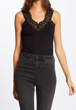Black tank top featuring a V-neck with intricate black lace trim, paired with high-waisted dark gray jeans for a cohesive look.