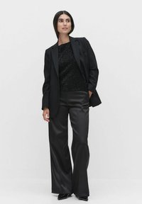 Sort blazer over en glitrende sort top, parret med brede sorte satinbukser. Farveskemaet er helt sort med skinnende teksturer.