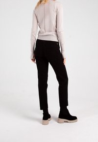 Czarne spodnie z fakturowanej tkaniny, o dopasowanym kroju. W połączeniu z jasnym swetrem oraz masywnymi czarnymi butami.