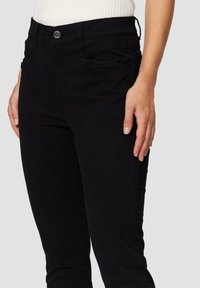 Zwarte katoen stretch jeans met een middelhoge taille, slim fit en voorzakken. Heeft een subtiele textuur en een metalen knoopsluiting.