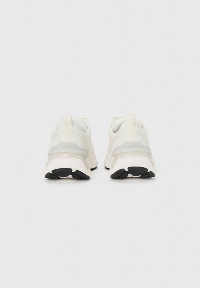 Scarpe sportive bianche con una parte superiore testurizzata e un accento grigio vicino al tallone. Suola in gomma nera con un motivo di battistrada distintivo.