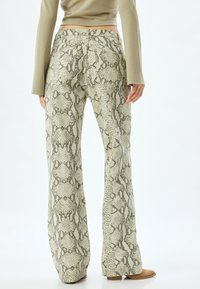 Pantalons évasés en imprimé serpent texturé présentant des nuances de vert et de beige. La vue arrière montre les poches et le détail de la ceinture.