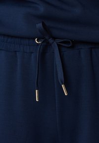 Marineblaue Jogginghosen mit glatter Textur, ausgestattet mit einem Kordelzugbund aus kontrastierendem geflochtenem Material und metallischen Enden.