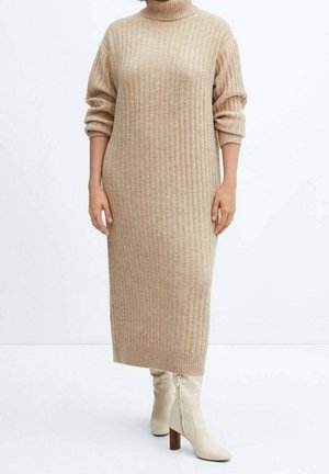 Mujer con vestido midi de punto beige acanalado con cuello alto y mangas largas, y botines de tacón en beige claro.