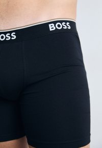 Schwarze Boxer-Briefs aus Stretchstoff. Mit einem weißen und goldenen Bund mit "BOSS"-Logo. Glatte Textur, enganliegendes Design.