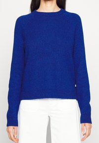Modrý pletený svetr s kulatým výstřihem, žebrovanými manžetami a lemem. Má mírně volný střih a texturovanou látku.