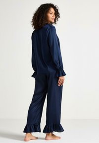 Navyblå satängpyjamas set som har långa ärmar och volangärmar, tillsammans med matchande byxor med volang längst ner. Mjuk textur, ledig passform.