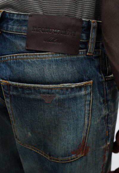 Mørkeblå denim jeans med let slitage, med et brunt læderbælte-label og et præget logo på baglommen.