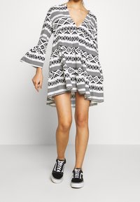 Robe à motifs noir et blanc avec un col en V, des manches évasées et une coupe fluide, assortie à des baskets noires. Ourlet court avec des imprimés géométriques.