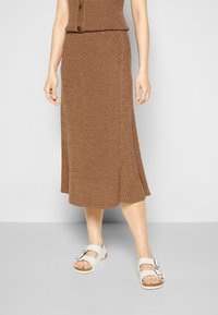 Saia midi castanha com pregas e um fundo godê, combinada com sandálias brancas com uma fivela prateada. Design simples e tecido texturizado.