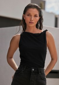 Top negro sin mangas con escote drapeado, hecho de tejido suave, combinado con unos jeans de mezclilla negros de cintura alta con bolsillos frontales.