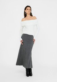 Suéter blanco de hombros descubiertos combinado con una falda maxi gris. La falda presenta una sutil textura moteada y una ligera amplitud, complementada con botas negras.