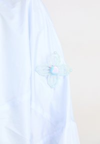Tessuto bianco con una spilla decorativa a forma di fiore, realizzata con perle e perline iridescenti, appuntata sulla manica.