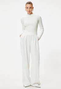 Un haut blanc à manches longues côtelées associé à un pantalon blanc taille haute à jambes larges. Les deux présentent une texture lisse et un design minimaliste.