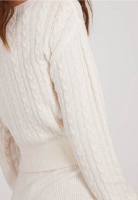 Kabelstrickpullover in Off-White, mit gerippten Bündchen und Saum. Weiche Textur mit passgenauer Silhouette, die detaillierte vertikale Muster zur Schau stellt.