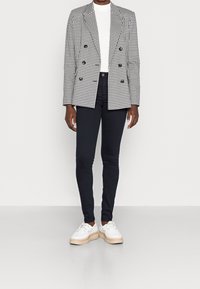 Blazer de doble botonadura en blanco y negro con estampado de houndstooth sobre un cuello de tortuga blanco, combinado con jeans skinny negros y zapatillas de plataforma blancas.