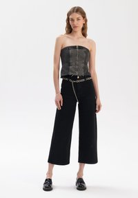 Zwarte denim strapless top met een sluiting aan de voorkant met knopen, gecombineerd met hoge zwarte wijde broekspijpen en een kettingriem.