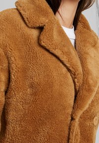 Brun faux fur frakke med en blød tekstur, indsnit krave og stort knapdetalje, med en afslappet pasform og enkelt design.