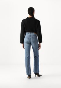 Juodas trumpas megztinis su ilgomis rankovėmis, derinamas su aukštu juosmeniu mėlynais džinsais, turinčiais tiesią koją ir dvi užpakalines kišenes.