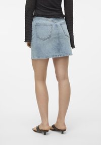 Ljusblå denimkjol med utsvängt snitt, mitt på låret, och två bakfickor. Kombinerad med mörka sandaler och en långärmad texturerad topp.